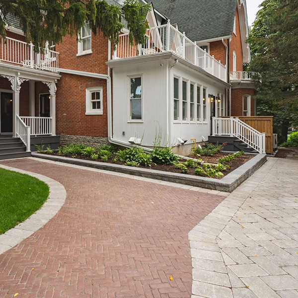 A red brick interlocked walkway leading up to a gothic revival style home with a white porch and sunroom
